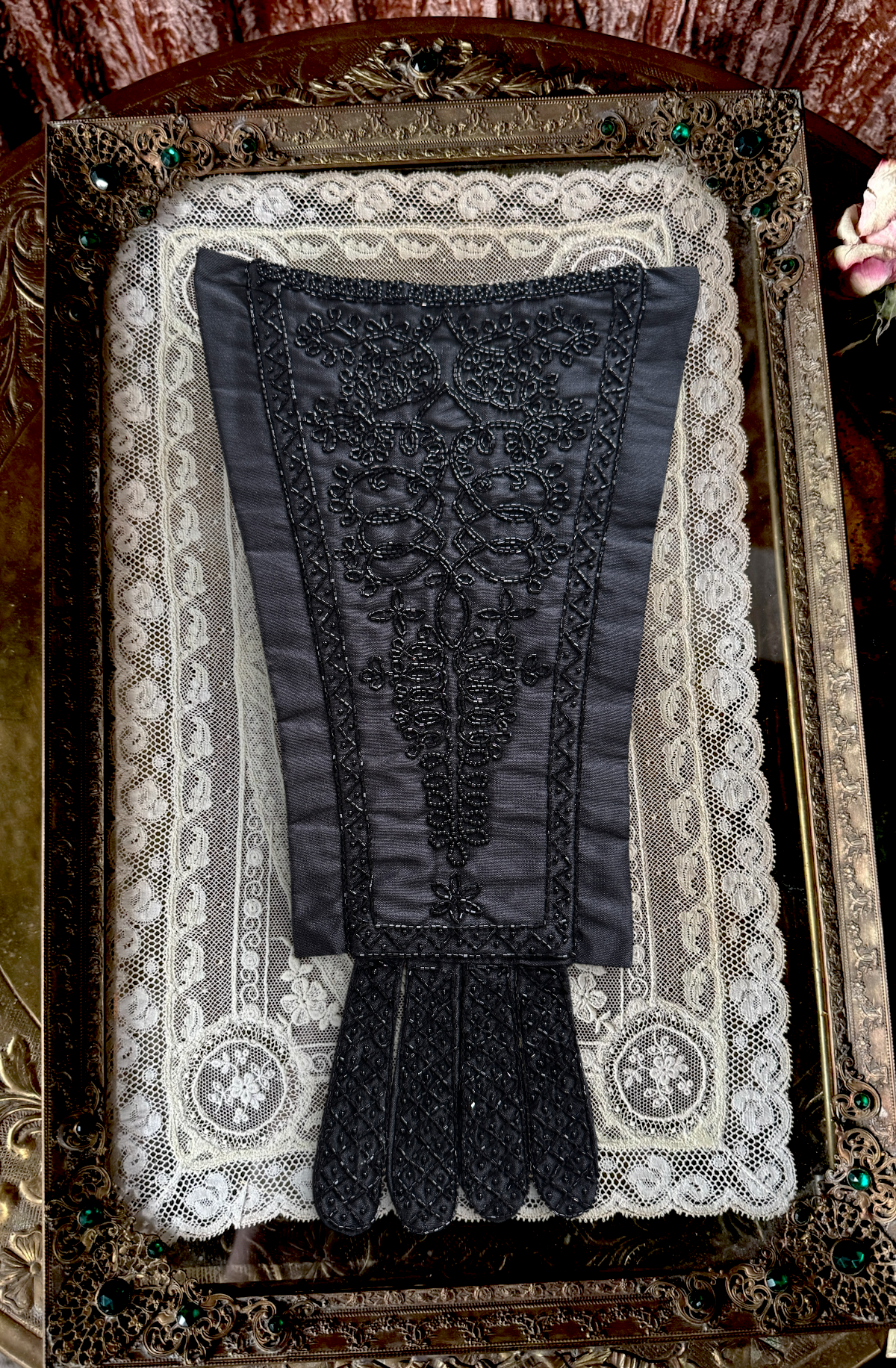 Black beaded mourning stomacher on a white lace background in an ornate frame