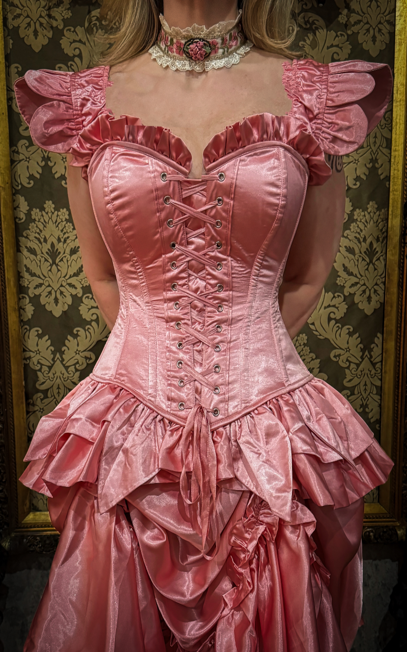 Pink Victorian-style corset with intricate details against a decorative wall.