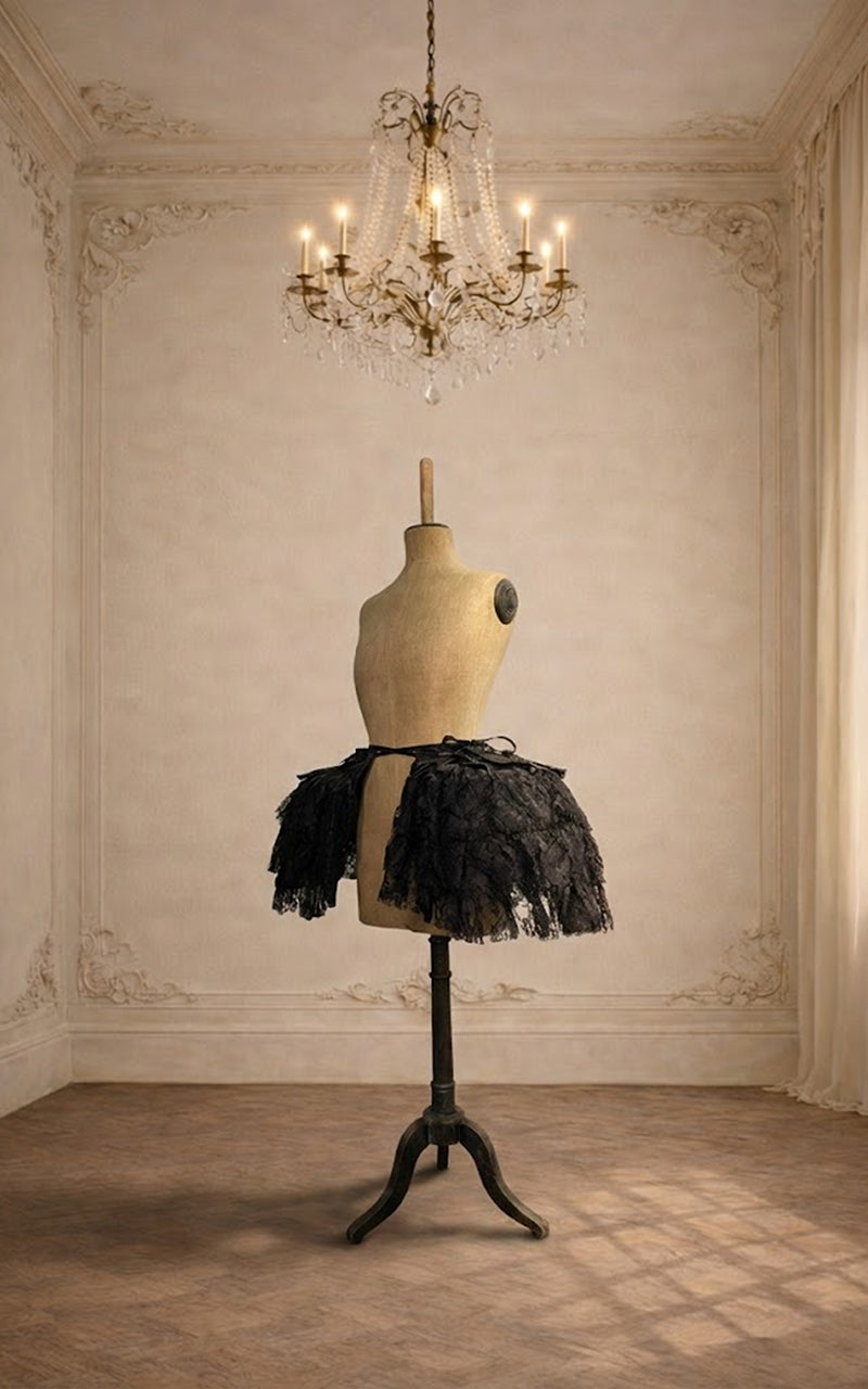 Mannequin wearing a black lace pannier in an elegant room with a chandelier.