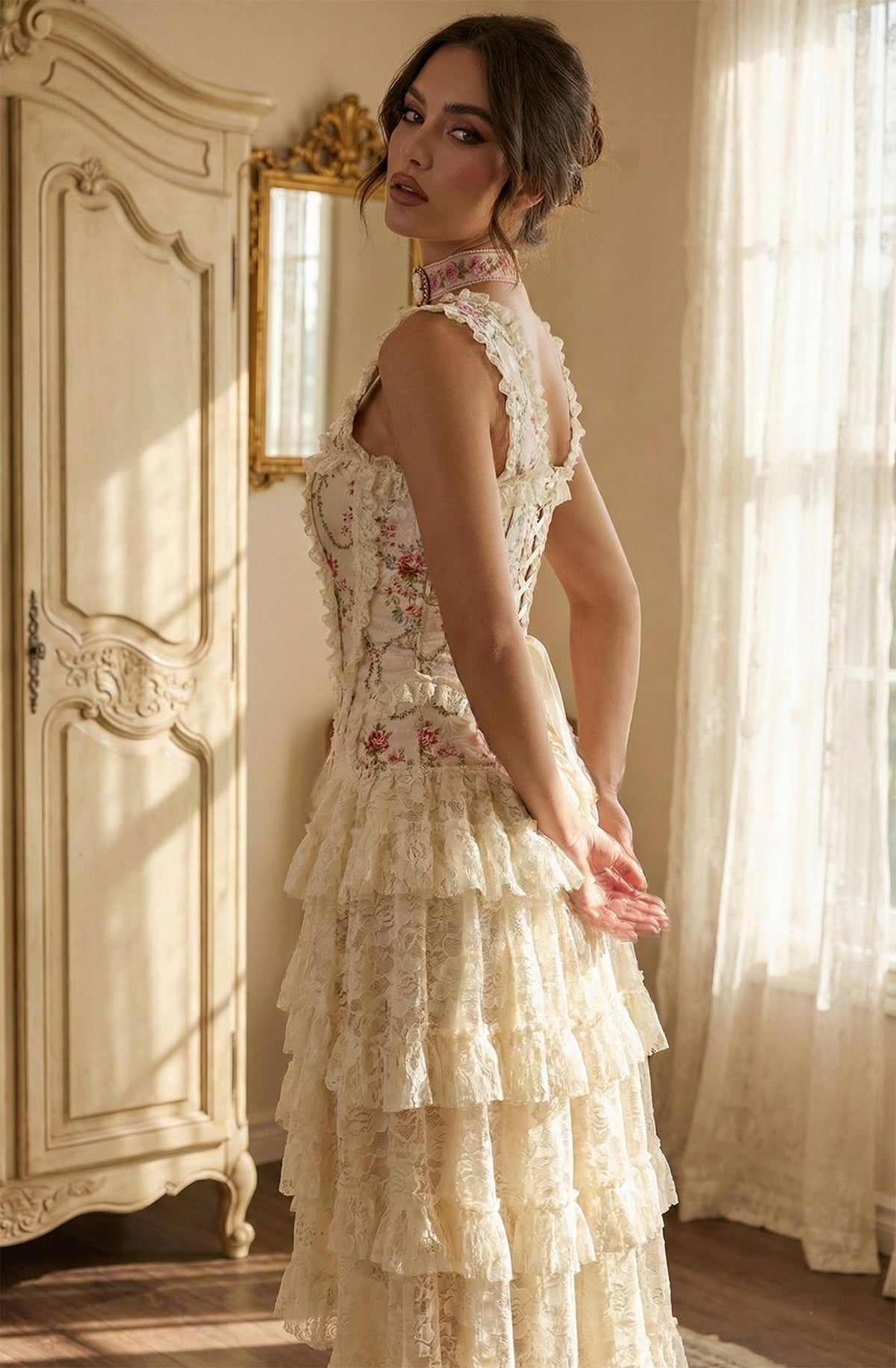 Woman in a floral lace corset dress standing in a softly lit room with a mirror and curtains.