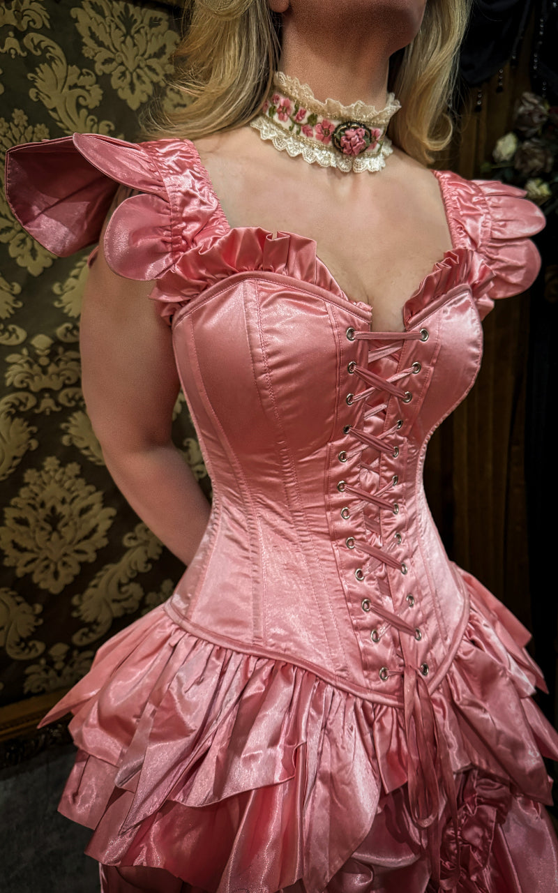 Pink fairy corset with floral necklace against a patterned wall.