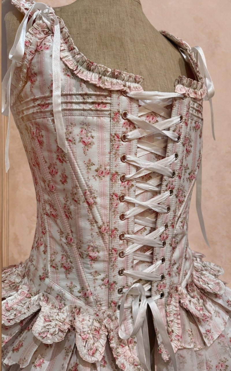 Vintage-style corset with floral patterns on a mannequin against a beige background